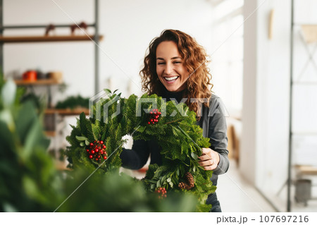 Attractive woman florist creating natural Christmas wreath in flower shop. Small business 107697216