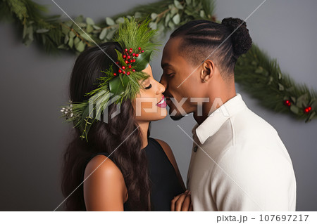Beautiful African American couple kissing under mistletoe. Christmas tradition Beautiful African American couple kissing under mistletoe. Christmas tradition 107697217