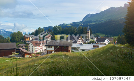 Churwalden village in Switzerland. Formerly Parpan. Beautiful swiss alpine countryside with a medieval bell tower and Rothorn mountain on background. 107697347