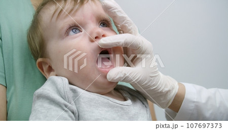 Doctor tries to check teeth of little boy in bright hospital ward 107697373