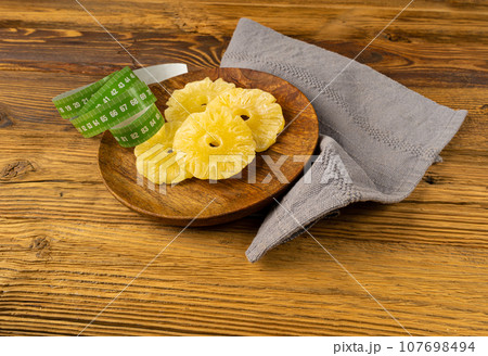 Dry Pineapple Rings on Wood Plate, Candy Pineapples, Dehydrated Yellow Sugar Fruit, Candied Fruits Circles Dry Pineapple Rings on Wood Plate, Candy Pineapples, Dehydrated Yellow Sugar Fruit, Candied Fruits Circles 107698494