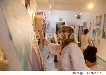 Side portrait of a creative mature blonde woman working on painting at her art studio. Education. Creative occupation 107699047