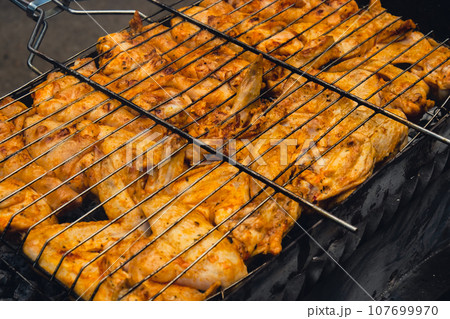 BBQ picnic time Roasted chicken legs and wings on grill. Grilling meat on outdoor grill grid tasty barbeque chicken steak with smoke flames juicy meat in the backyard 107699970