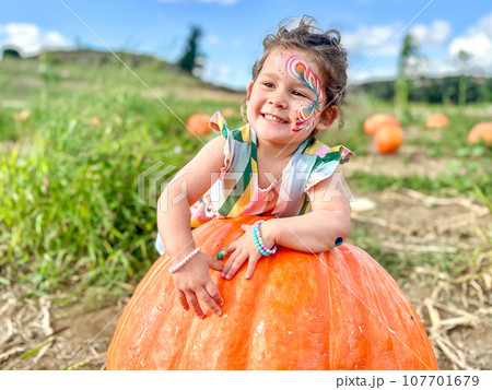Little girl picking pumpkins on Halloween pumpkin patch. Child playing in field of squash. Little girl picking pumpkins on Halloween pumpkin patch. Child playing in field of squash. 107701679