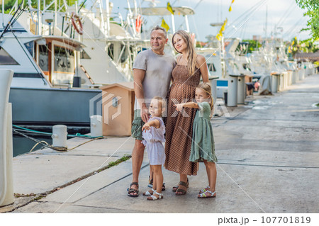 A happy, mature couple over 40 with their two daughters enjoying a leisurely walk on the waterfront, their joy evident as they embrace the journey of pregnancy later in life 107701819