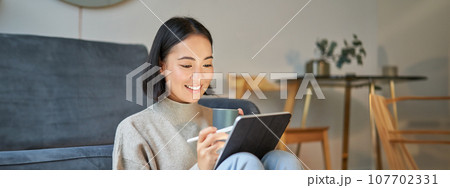 Smiling korean woman sitting with tablet and pen, drawing and scatching her new project or design, working from home 107702331
