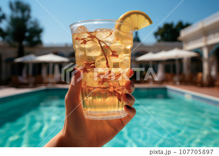 Lemonade in a glass in a person's hand against the background of a villa or hotel pool. The concept of summer holidays and recreation 107705897