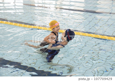 プールで女の子の手を引く水泳コーチ 107709429