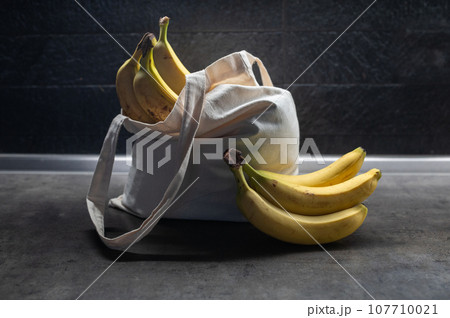 Sweet Ripe yellow fruit bananas in shopping bag on table. Dark background. Healthy tropical food 107710021