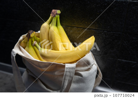 Sweet Ripe yellow fruit bananas in shopping bag on table. Dark background. Healthy tropical food 107710024