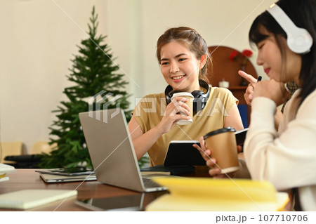 Two cheerful female colleague looking at laptop, working on a new project in creative coworking office 107710706