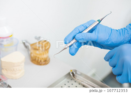 A dentist's hands holding dental instruments for teeth treatment, with jaw models in the background. 107712353
