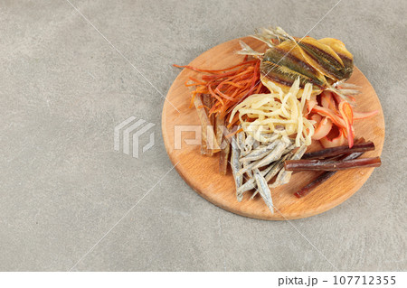 Different types of dried fish and squid on a round wooden board. Beer snack. Snack for men's company. Different types of dried fish and squid on a round wooden board. Beer snack. Snack for men's company. 107712355