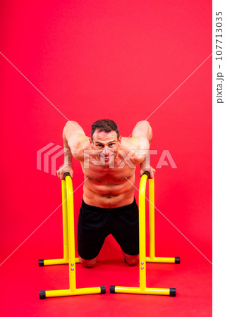 Front and side view photo of an strong young man exercising on parallel bars in studio. 107713035