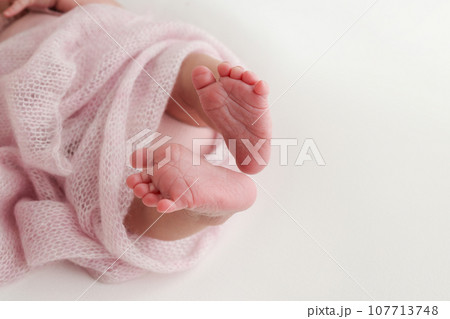 Close-up of tiny, cute, bare toes, heels and feet of a newborn girl, boy. Baby foot on pink soft coverlet, blanket. Detail of a newborn baby legs. Macro horizontal professional studio photo.  107713748