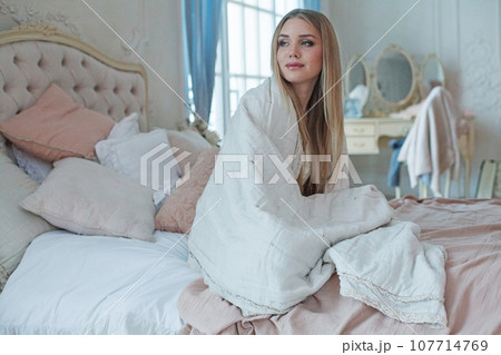 Happy young woman with long blonde hair sitting in bed in the morning 107714769