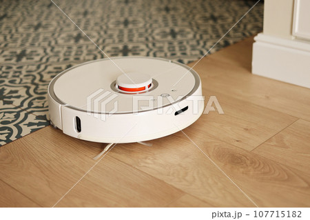 Wireless autonomous smart robotic vacuum cleaner is vacuuming floor with modern tiles at living room. Self-propelled cleaning robot. Floor cleaning system. Household remote control appliances. 107715182
