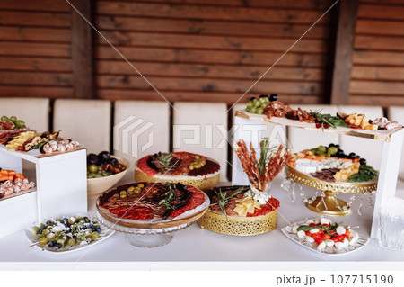 Appetizers table with meat and cheese. Salami, sausages, variation of cheese, grapes, tomatoes, green olives, rosemary, tapas on wooden plates. Snack finger food meal for wine, starter. 107715190