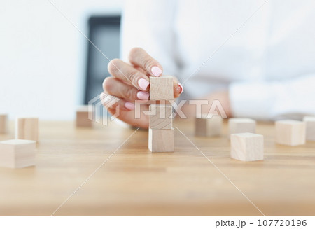 Female hand builds tower from wooden cubes 107720196