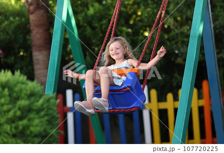 Happy little girl swinging on swing concept Happy little girl swinging on swing concept 107720225