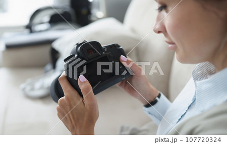 Woman holds black professional camera in her hands 107720324