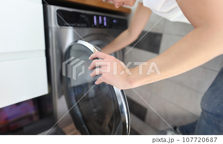 Woman opens door of washing machine closeup 107720687