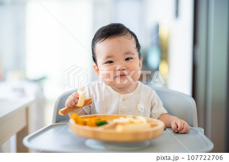 離乳食後期でをつかみ食べをしてご機嫌な生後9か月の赤ちゃん 107722706