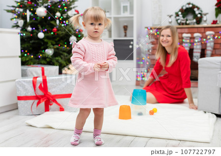 A little girl in a pink dress stands against the backdrop of a Christmas tree 107722797