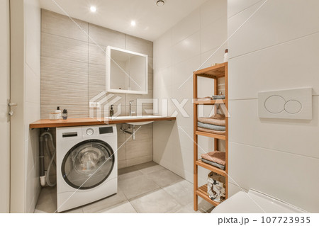 a small laundry room with a washer and dryer in the corner, there is a wooden shelf on the wall a small laundry room with a washer and dryer in the corner, there is a wooden shelf on the wall 107723935