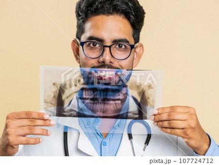 Indian young doctor orthodontist man examines a panoramic x-ray picture of the jaw teeth stomatology Indian young doctor orthodontist man examines a panoramic x-ray picture of the jaw teeth stomatology 107724712
