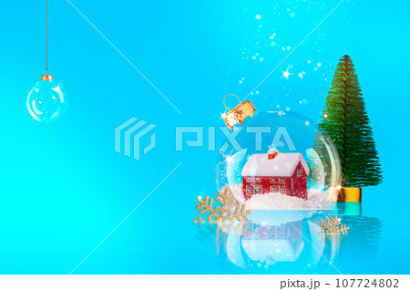 Christmas blue background with transparent snow globe, inside with house and Christmas tree. New Year background, winter composition from glass ball Christmas blue background with transparent snow globe, inside with house and Christmas tree. New Year background, winter composition from glass ball 107724802