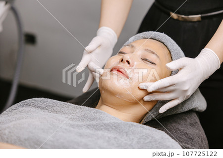 Woman facial massage face skin treatment with natural essence herbal extract moisturising cream in beauty spa clinic. 107725122