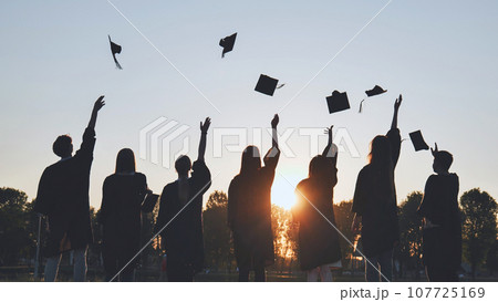 Silhouettes of Happy college graduates tossing their caps up at sunset. Silhouettes of Happy college graduates tossing their caps up at sunset. 107725169