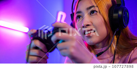 You win. Gamer using joystick controller plays online video game with computer neon lights she winning, woman wear gaming headphones playing live stream esports games console at home celebrating win You win. Gamer using joystick controller plays online video game with computer neon lights she winning, woman wear gaming headphones playing live stream esports games console at home celebrating win 107727898