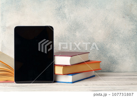 Digital tablet with a stack of books on gray background 107731807