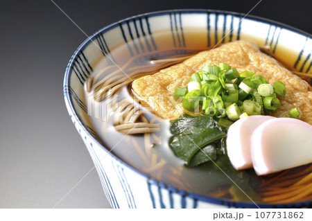 油揚げ、かまぼこ、ワカメ、葱が乗ったきつね蕎麦を黒背景で撮影 油揚げ、かまぼこ、ワカメ、葱が乗ったきつね蕎麦を黒背景で撮影 107731862