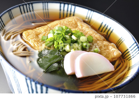 油揚げ、かまぼこ、ワカメ、葱が乗ったきつね蕎麦を黒背景で撮影 油揚げ、かまぼこ、ワカメ、葱が乗ったきつね蕎麦を黒背景で撮影 107731866