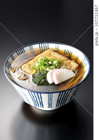 油揚げ、かまぼこ、ワカメ、葱が乗ったきつね蕎麦を黒背景で撮影 油揚げ、かまぼこ、ワカメ、葱が乗ったきつね蕎麦を黒背景で撮影 107731867