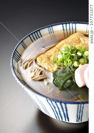 油揚げ、かまぼこ、ワカメ、葱が乗ったきつね蕎麦を黒背景で撮影 油揚げ、かまぼこ、ワカメ、葱が乗ったきつね蕎麦を黒背景で撮影 107731877