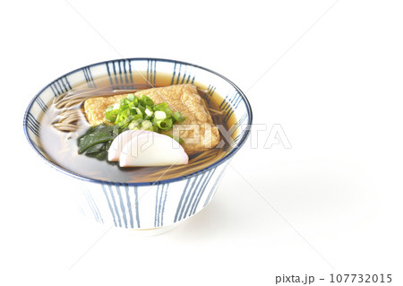 油揚げ、かまぼこ、ワカメ、葱が乗ったきつね蕎麦を白背景で撮影 107732015