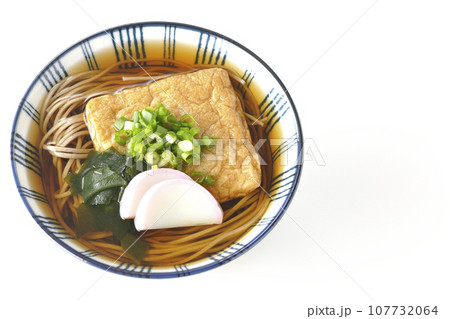 油揚げ、かまぼこ、ワカメ、葱が乗ったきつね蕎麦を白背景で俯瞰撮影 107732064