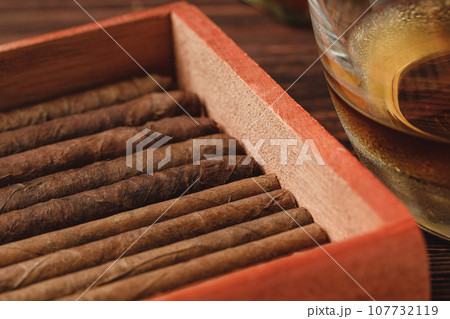 Red wooden box with rolled cigars on wooden table close up 107732119
