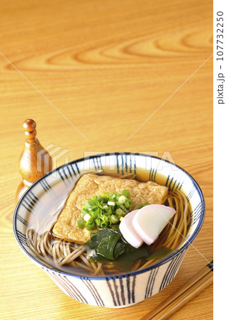 油揚げ、かまぼこ、ワカメ、葱が乗ったきつね蕎麦と瓢箪型の唐辛子入れ 107732250