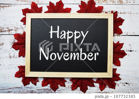 Happy November text on blackboard decorated with red maple leaves on wooden background 107732385