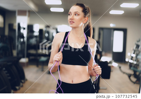 Portrait of a fit girl with jumping rope standing in a gym Portrait of a fit girl with jumping rope standing in a gym 107732545