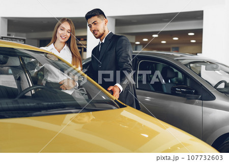 Man car dealer showing a woman buyer a new car Man car dealer showing a woman buyer a new car 107732603