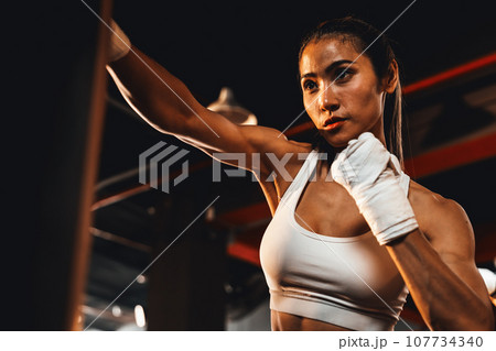 Asian female Muya Thai boxer training, wrapped hand punching. Impetus 107734340