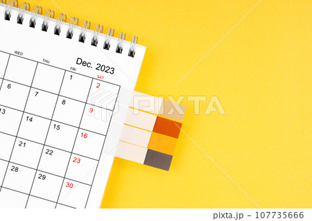 The December 2023 Monthly desk calendar and blank adhesive note on yellow background. 107735666