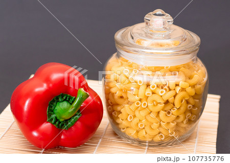 Uncooked Chifferi Rigati Pasta in Glass Jar with Red Bell Pepper on Bamboo Mat Uncooked Chifferi Rigati Pasta in Glass Jar with Red Bell Pepper on Bamboo Mat 107735776