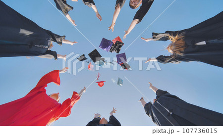 Happy college graduates standing in a circle tossing colorful hats up. 107736015